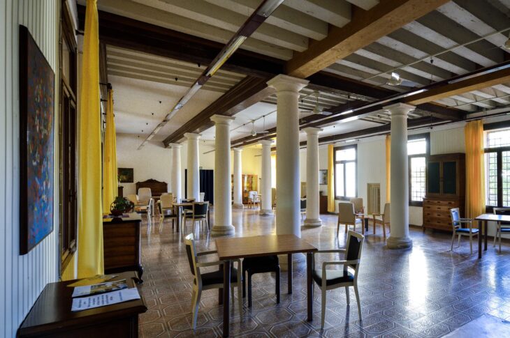 Ampia sala comune con tavoli, sedie, colonne e spazi dedicati alla socializzazione degli ospiti.