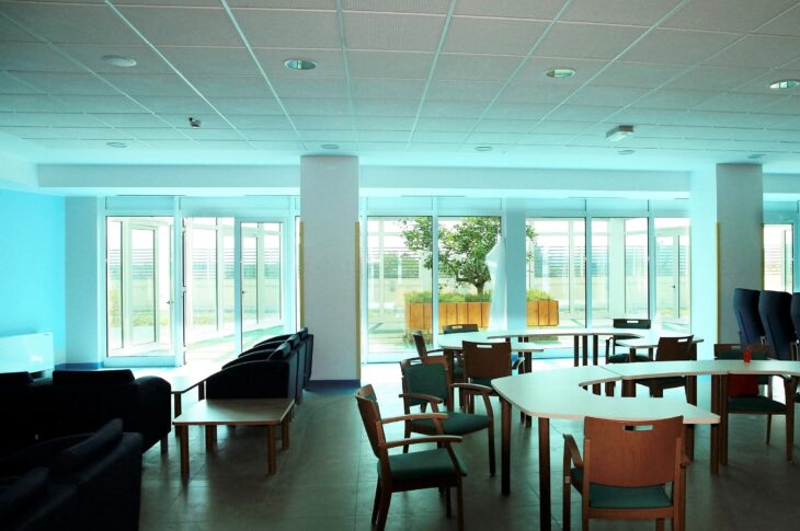 Sala soggiorno luminosa con tavoli, poltrone e ampie vetrate affacciate sull'esterno.